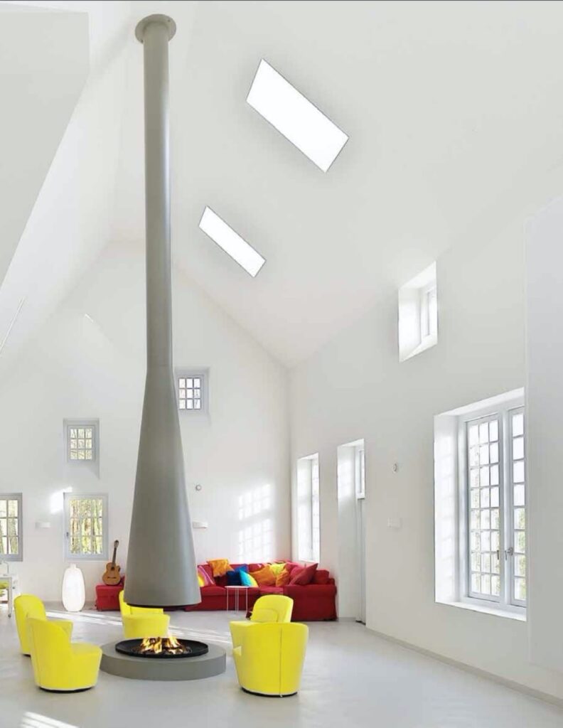 Ronde, moderne houthaard, centraal in woonkamer met stoelen eromheen.